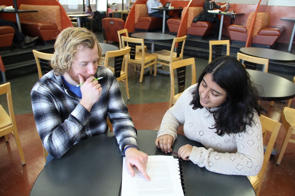 A man and a woman sit at a table and look over a piece of writing.